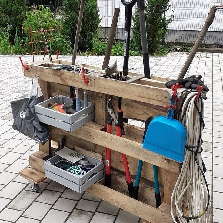 Garage Storage for Lawn Equipment: 7 Ideas That Actually Fit 8 A wooden pallet storage cart holding various garden tools and grey plastic bins on a patio.
