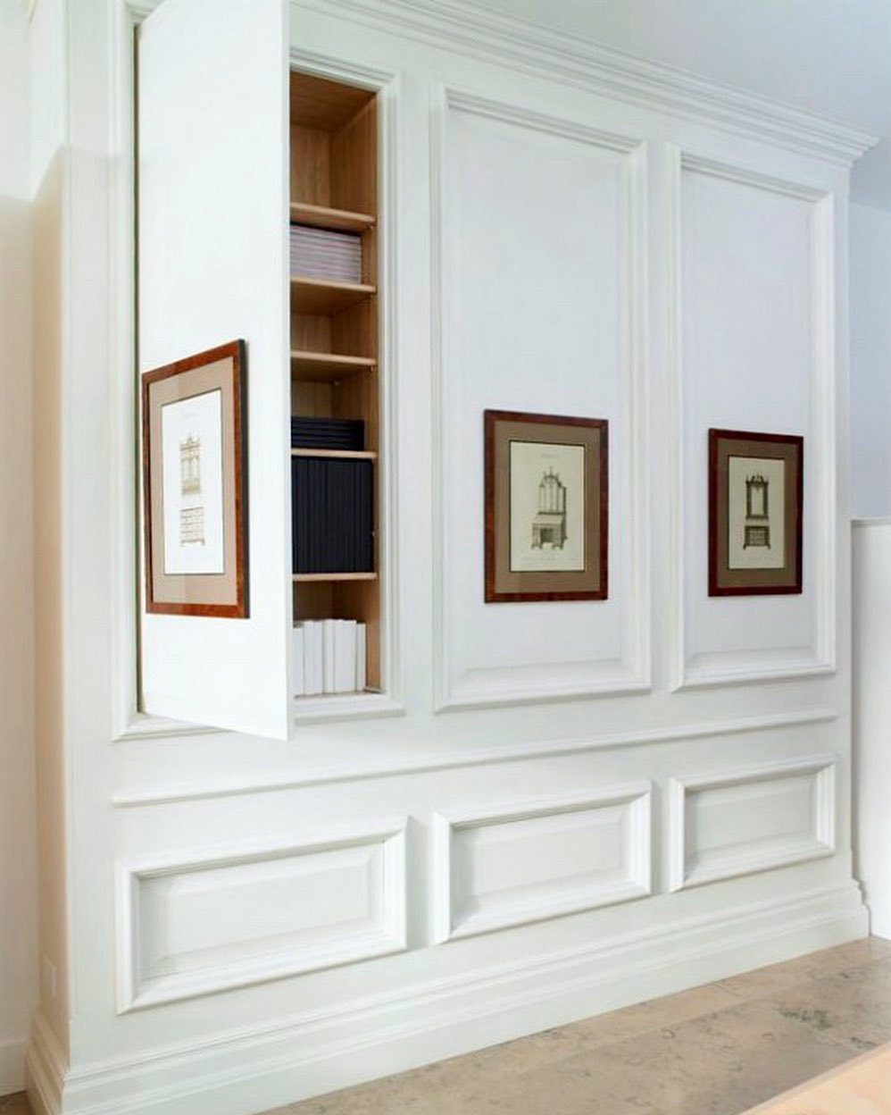 9 Hidden Storage Wall Ideas for a Cleaner Home 9 White paneled wall with an open secret door revealing built-in wooden bookshelves filled with books.