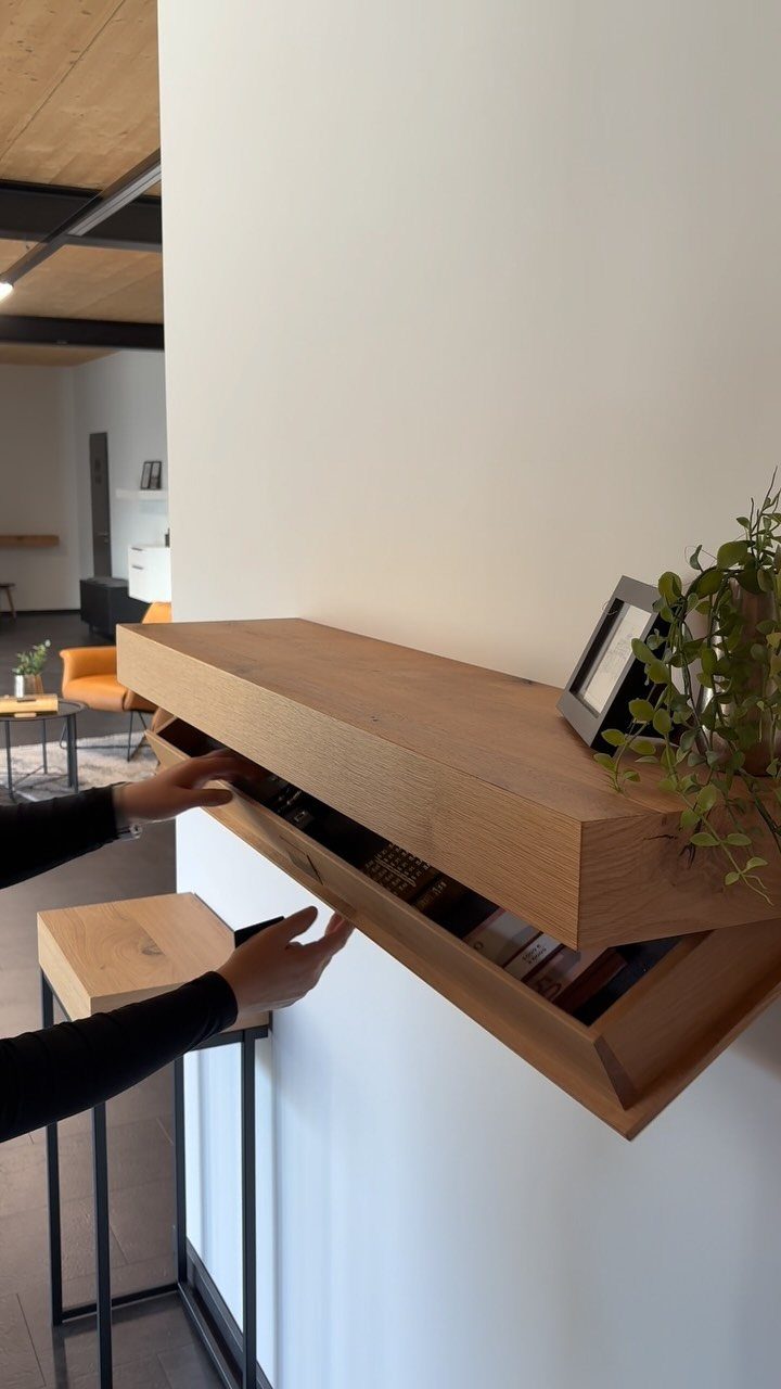 9 Hidden Storage Wall Ideas for a Cleaner Home 7 Hands opening a wooden floating shelf that reveals a hidden storage compartment on a white wall.
