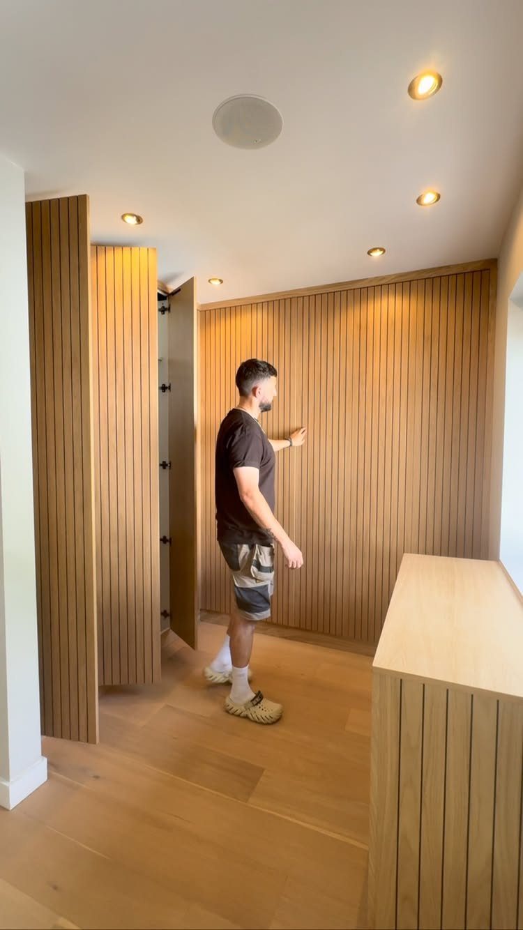9 Hidden Storage Wall Ideas for a Cleaner Home 10 A man opens a section of a vertical wooden slat wall to reveal hidden storage.