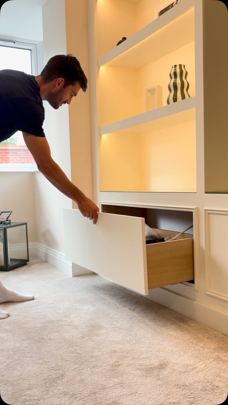9 Hidden Storage Wall Ideas for a Cleaner Home 6 A man opening a large white drawer integrated into a wall unit with illuminated shelving.