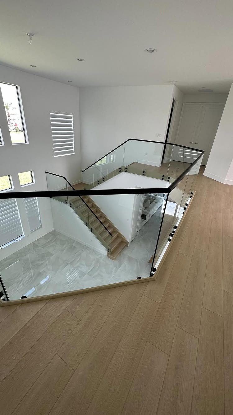 Home Stairs Design: 12 Ideas from Glass Treads to Built-In Storage 3 A modern wooden staircase enclosed by clear glass railings and black handrails in a bright room.