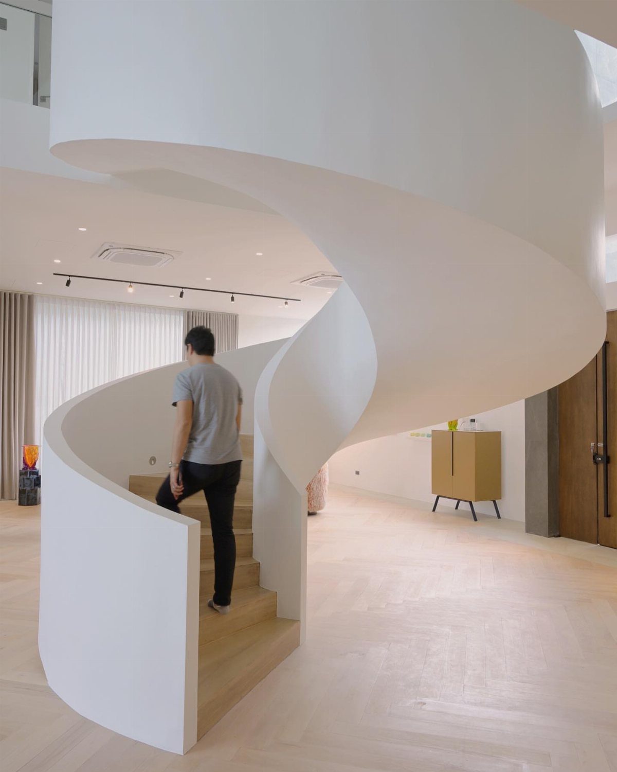 Home Stairs Design: 12 Ideas from Glass Treads to Built-In Storage 9 A white sculptural ribbon staircase curves through a bright, minimalist modern room with light wood floors.