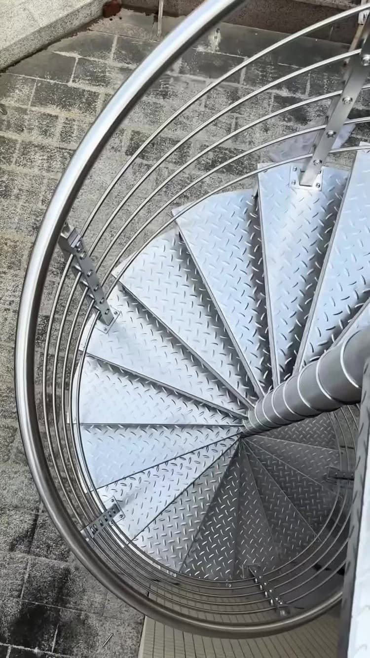 Home Stairs Design: 12 Ideas from Glass Treads to Built-In Storage 2 A top-down view of a silver metal spiral staircase with textured diamond-plate steps.