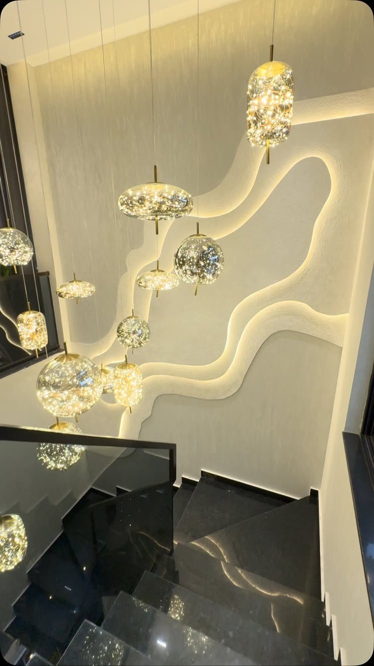 Home Stairs Design: 12 Ideas from Glass Treads to Built-In Storage 8 Modern black stairs with wavy backlit walls and hanging textured glass pendant lights.