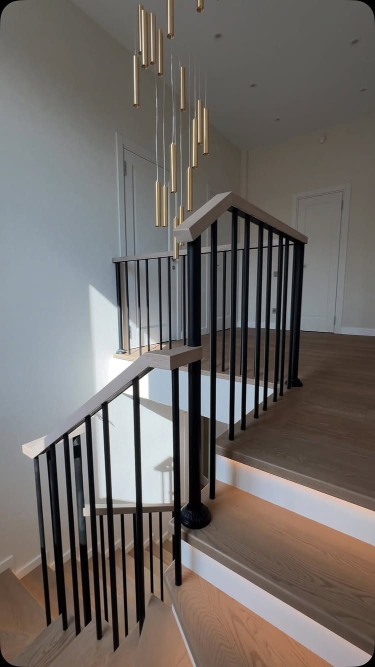 Home Stairs Design: 12 Ideas from Glass Treads to Built-In Storage 11 Modern wooden stairs with black metal railings and a long gold cylindrical pendant light hanging above.