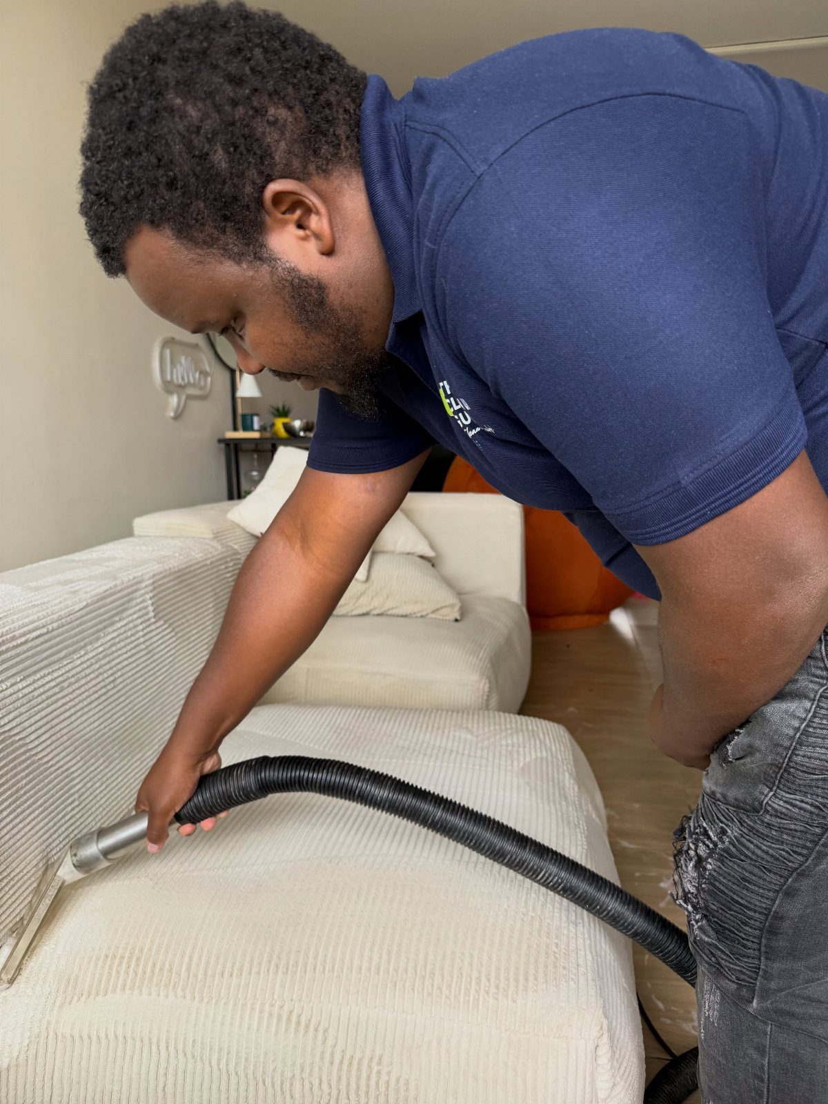 A man uses a vacuum cleaner attachment to clean the fabric of a light-colored sofa.