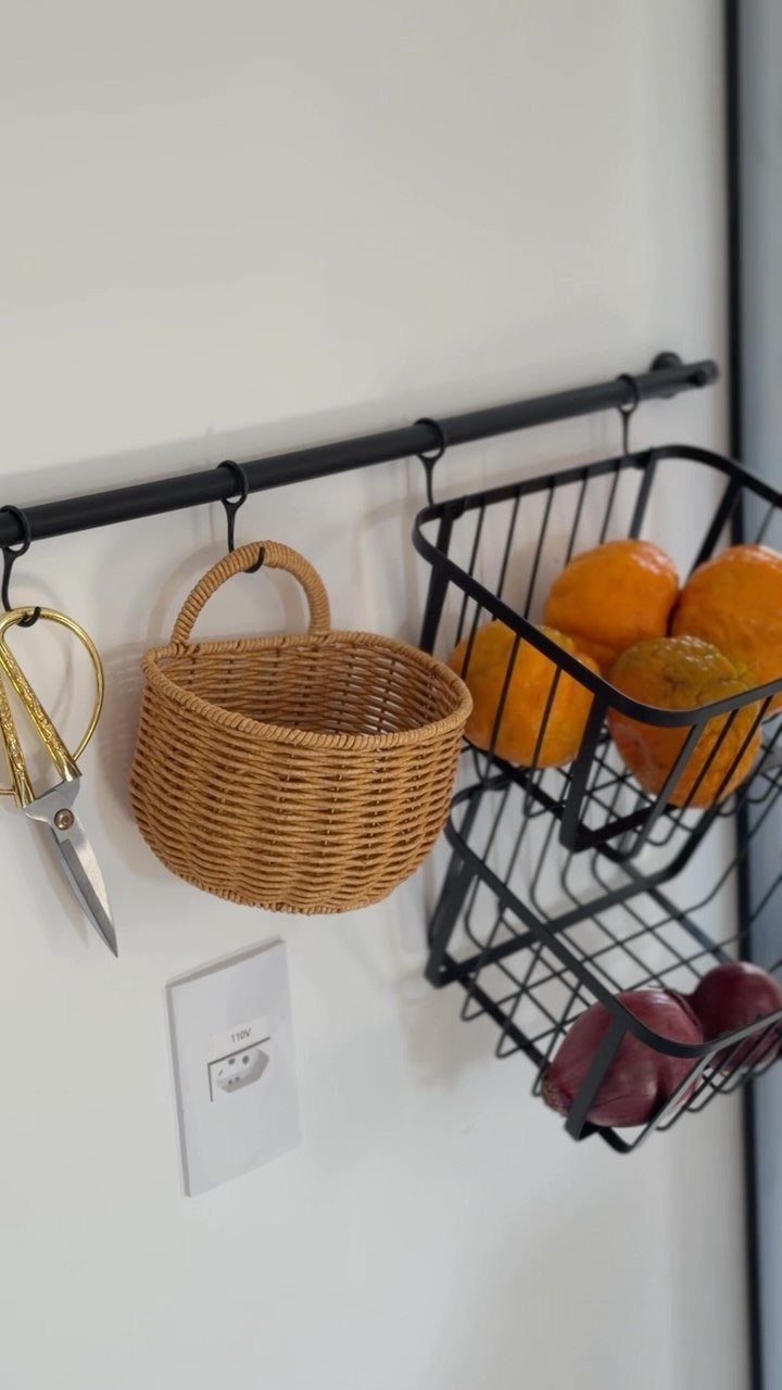 Hanging wicker and wire baskets containing fruit on a black wall-mounted rod.