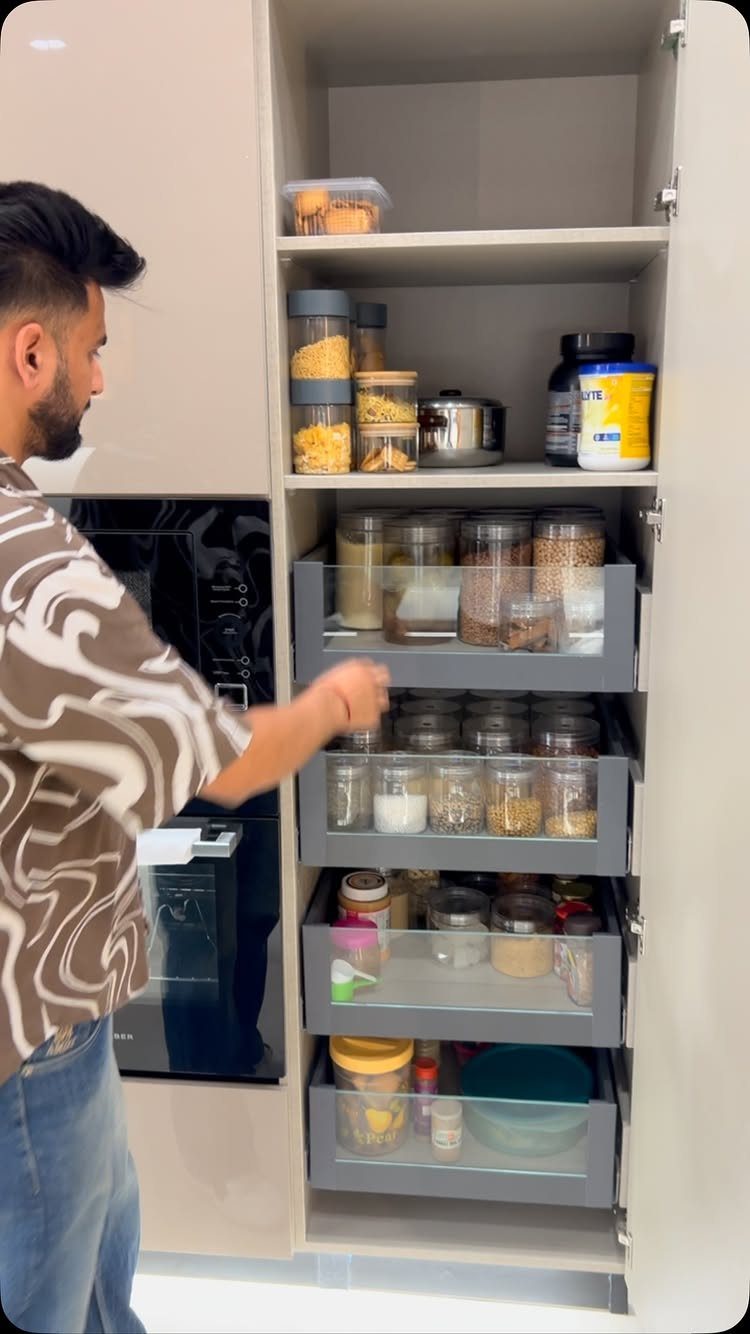 A man reaches into a tall pantry filled with grey pull-out drawers containing various food containers.