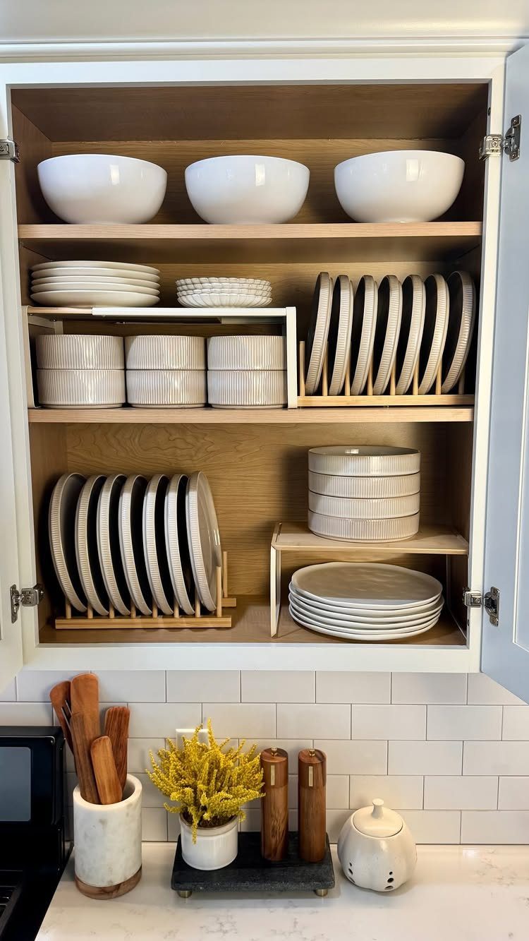Organized white ceramic bowls and plates arranged neatly on wooden kitchen cabinet shelves.