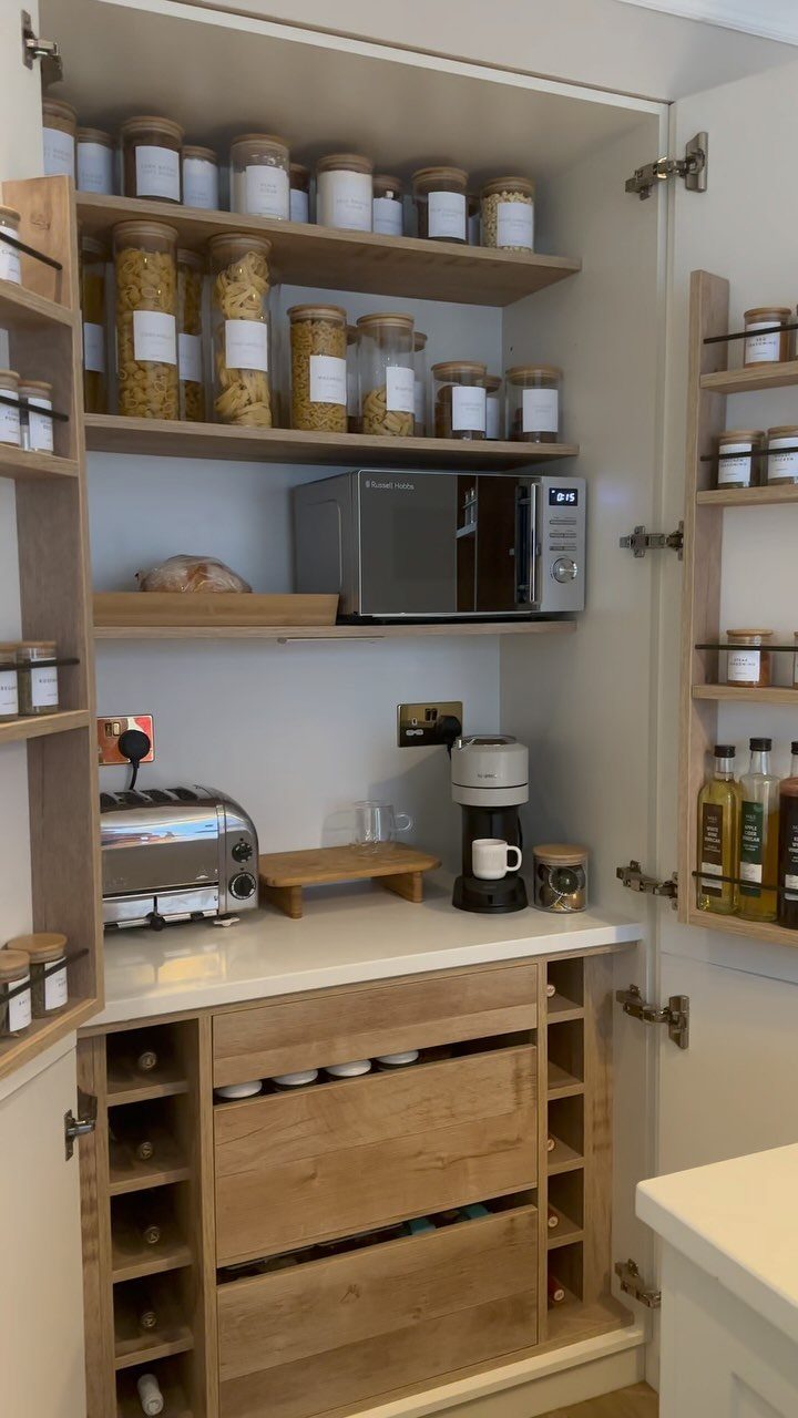 An open pantry with wooden shelves, glass canisters, a microwave, toaster, and spice racks on the doors.