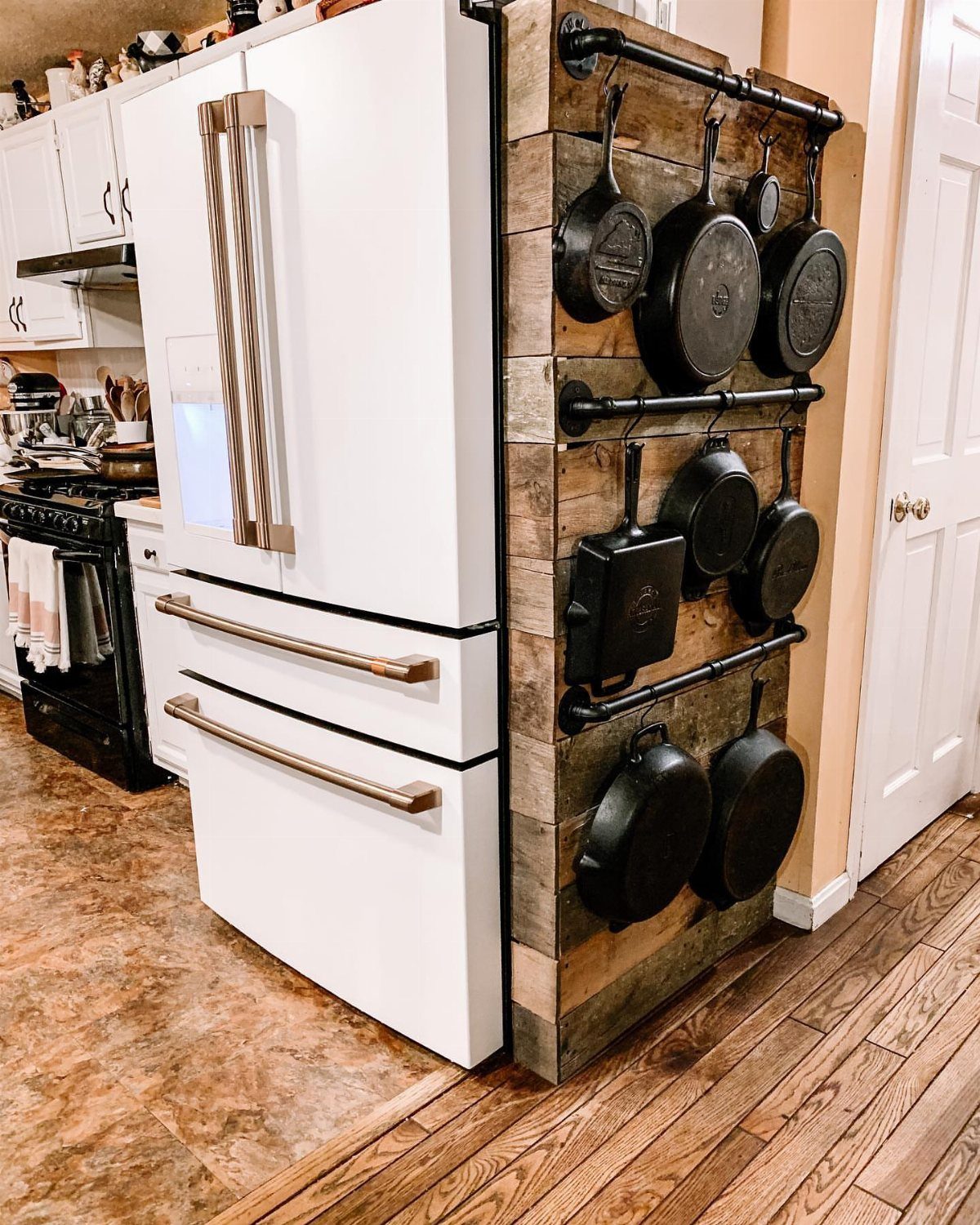 9 Kitchen Tools Organization Ideas for Cabinets, Drawers & Walls 7 Black cast iron pans hanging from a rustic wooden wall mounted pot rack next to a refrigerator.