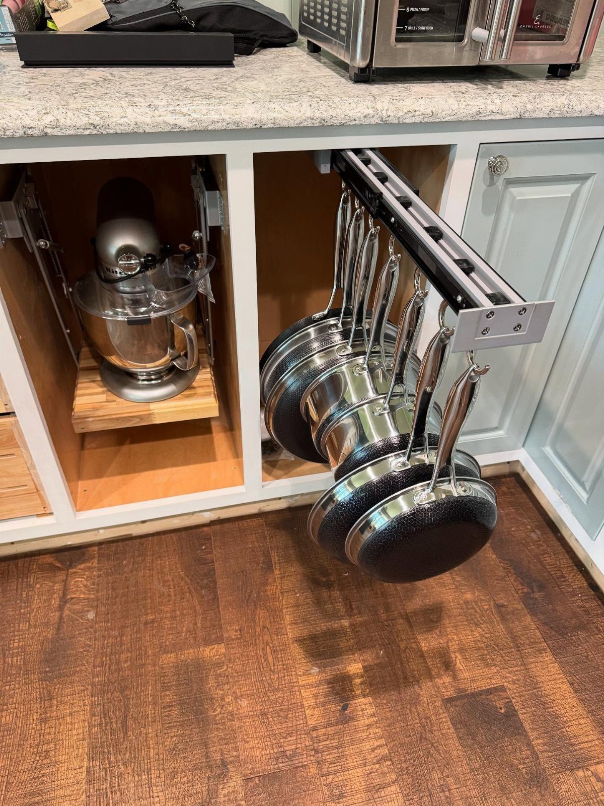 9 Kitchen Tools Organization Ideas for Cabinets, Drawers & Walls 3 A pull-out kitchen cabinet drawer containing several hanging black frying pans and pots.