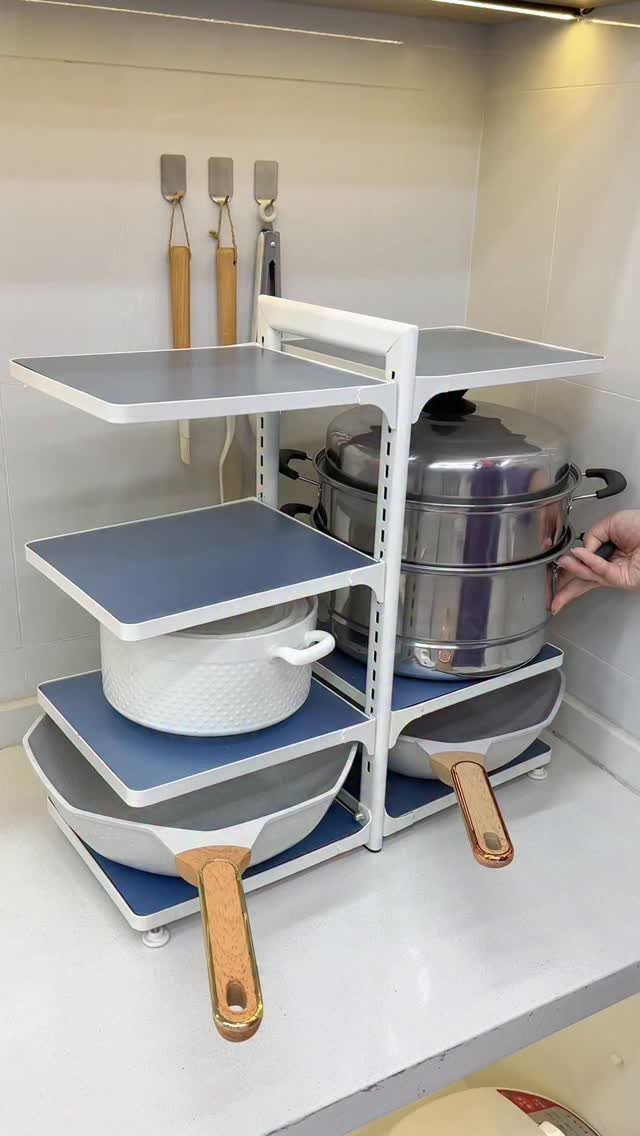 9 Kitchen Tools Organization Ideas for Cabinets, Drawers & Walls 9 White metal tiered organizer rack holding various stainless steel pots and pans on a kitchen counter.