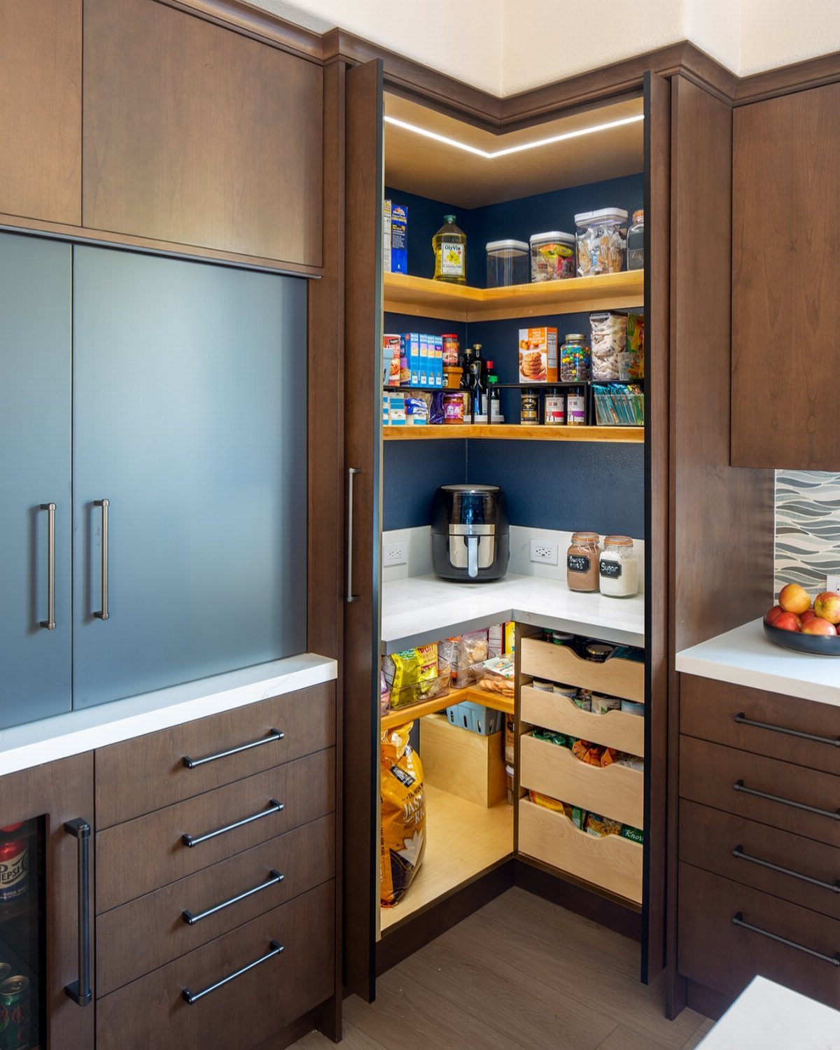 Kitchen with Hidden Pantry: 8 Ideas That Blend Right In 6 An open corner pantry with blue walls, wooden shelves, and various food items stored inside.