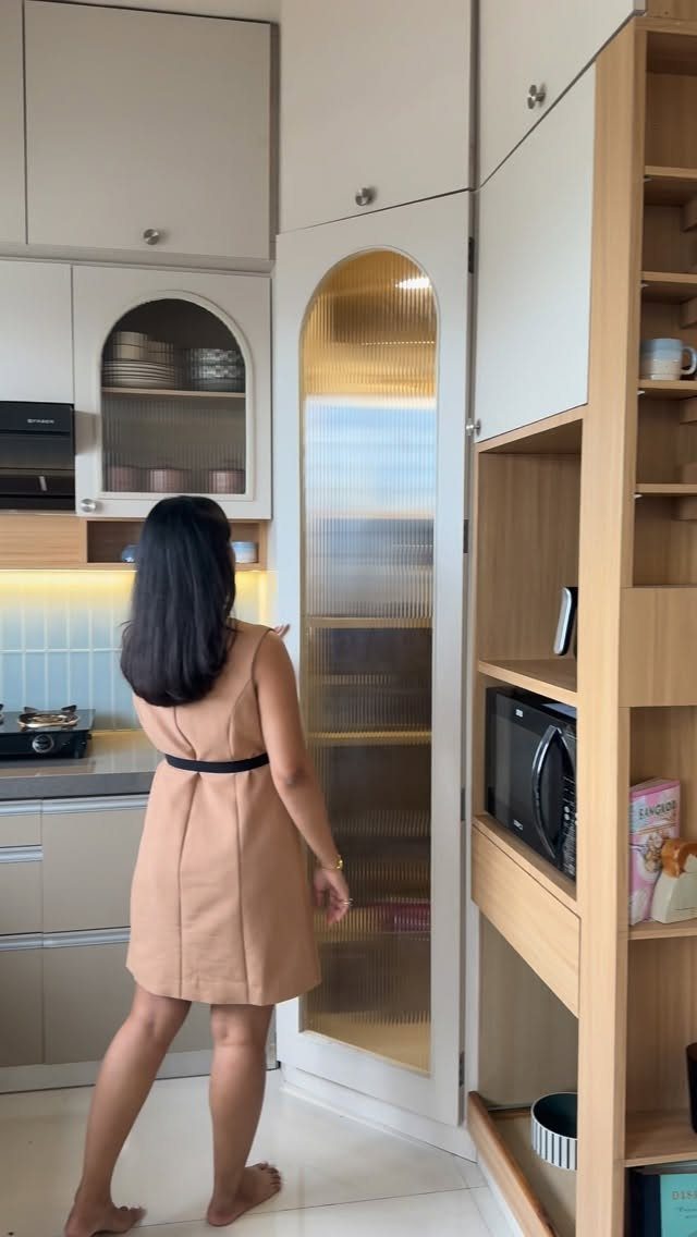 Kitchen with Hidden Pantry: 8 Ideas That Blend Right In 9 A woman stands in a kitchen looking at a tall cabinet with a fluted glass pantry door.