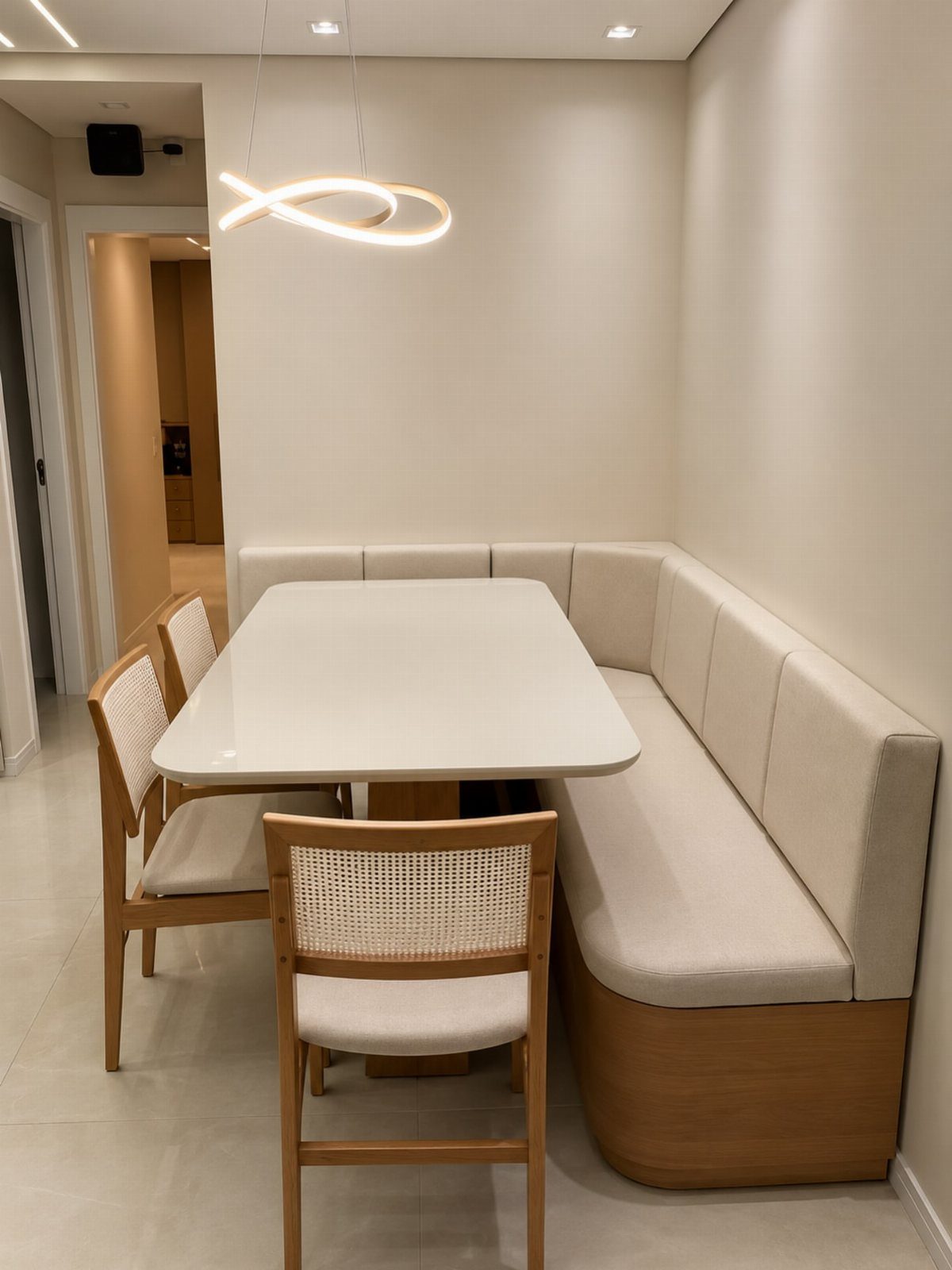 A modern dining set with a white table, cane chairs, and a built-in L-shaped bench.