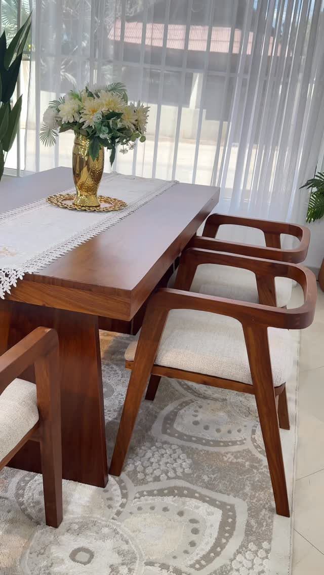 Wooden dining table with white flowers and lace runner on a patterned rug.