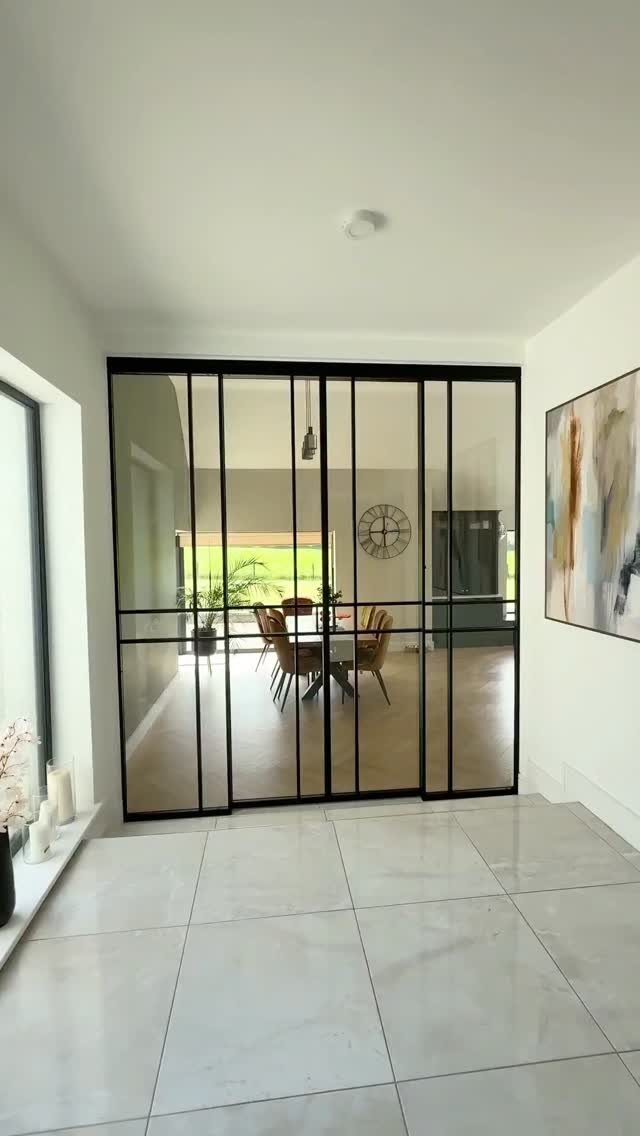 Black-framed glass sliding doors separating a hallway from a bright dining room.