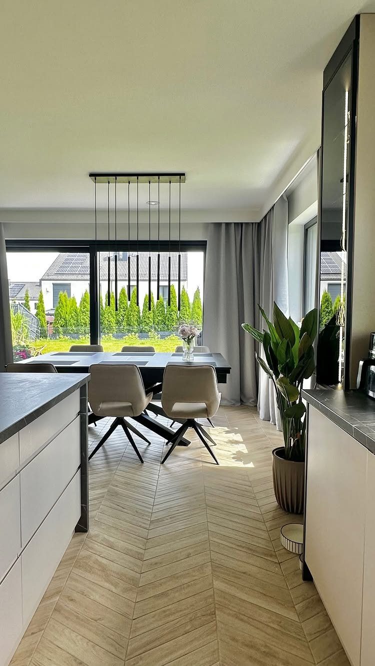 Light-colored herringbone wood flooring in a modern dining room with a large window.