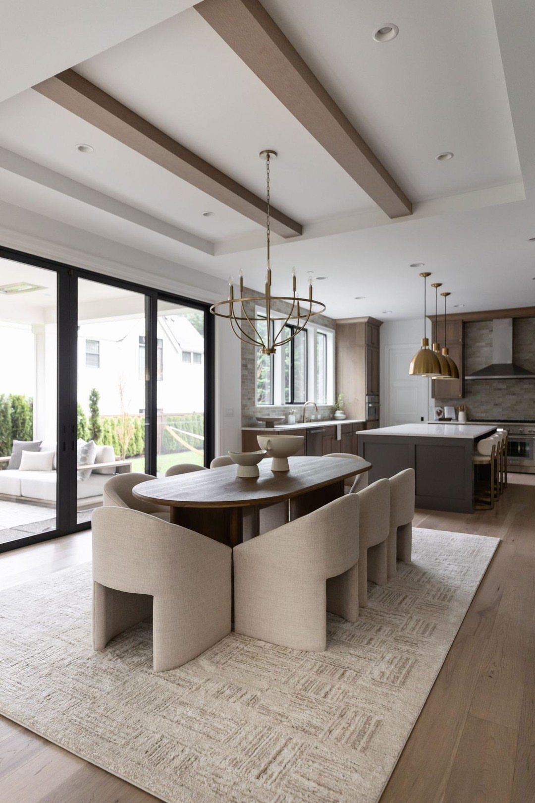 Dining area with wooden table and cream chairs overlooking a modern kitchen and patio.