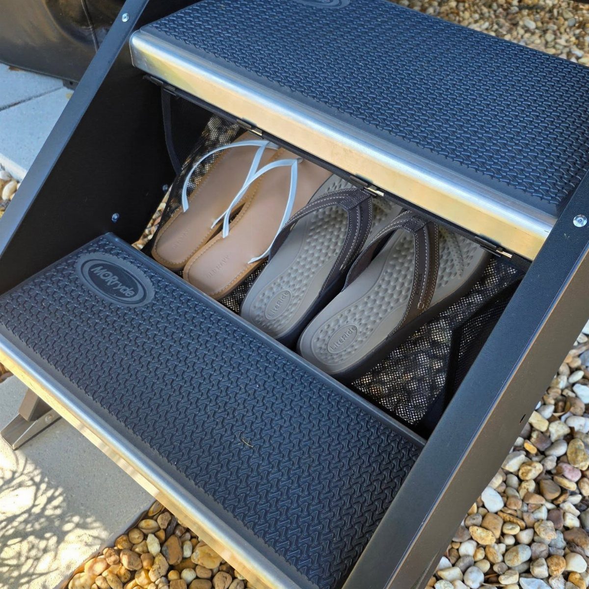 RV Shoe Storage: 6 Ideas That Save Space and Sanity 6 Tan and grey flip-flops stored in a compartment under black textured RV entry steps.