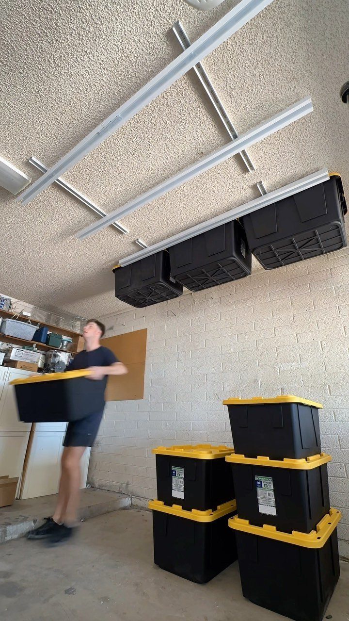 14 Shed Organization Ideas for a Tidy, Functional Space 3 A person carries a black bin near ceiling-mounted storage racks holding several black containers.