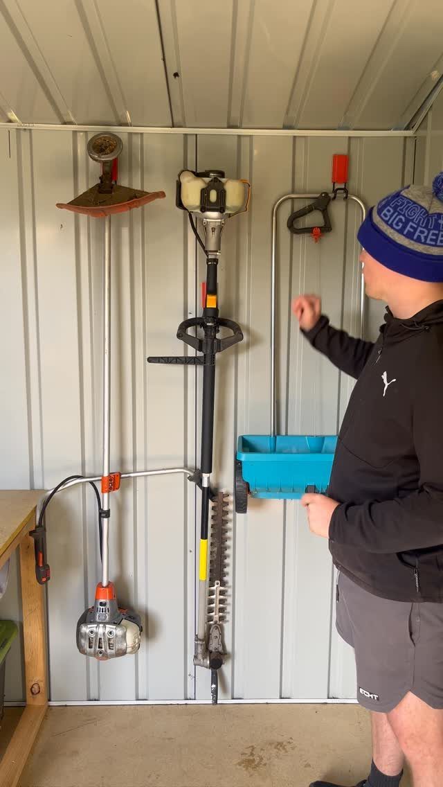 14 Shed Organization Ideas for a Tidy, Functional Space 5 A man stands in a shed looking at long-handled garden tools hanging on the wall.