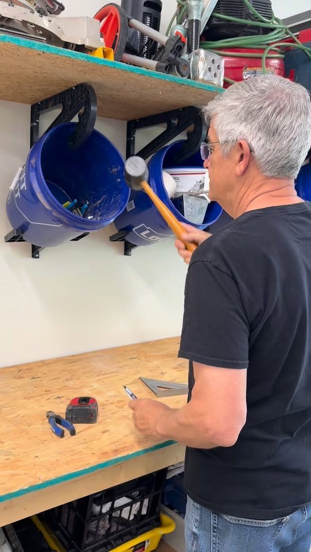 13 Shop Tool Storage Ideas for Pegboard, Carts and Cabinets 8 A man holding a mallet in a workshop with blue buckets mounted on wall brackets.