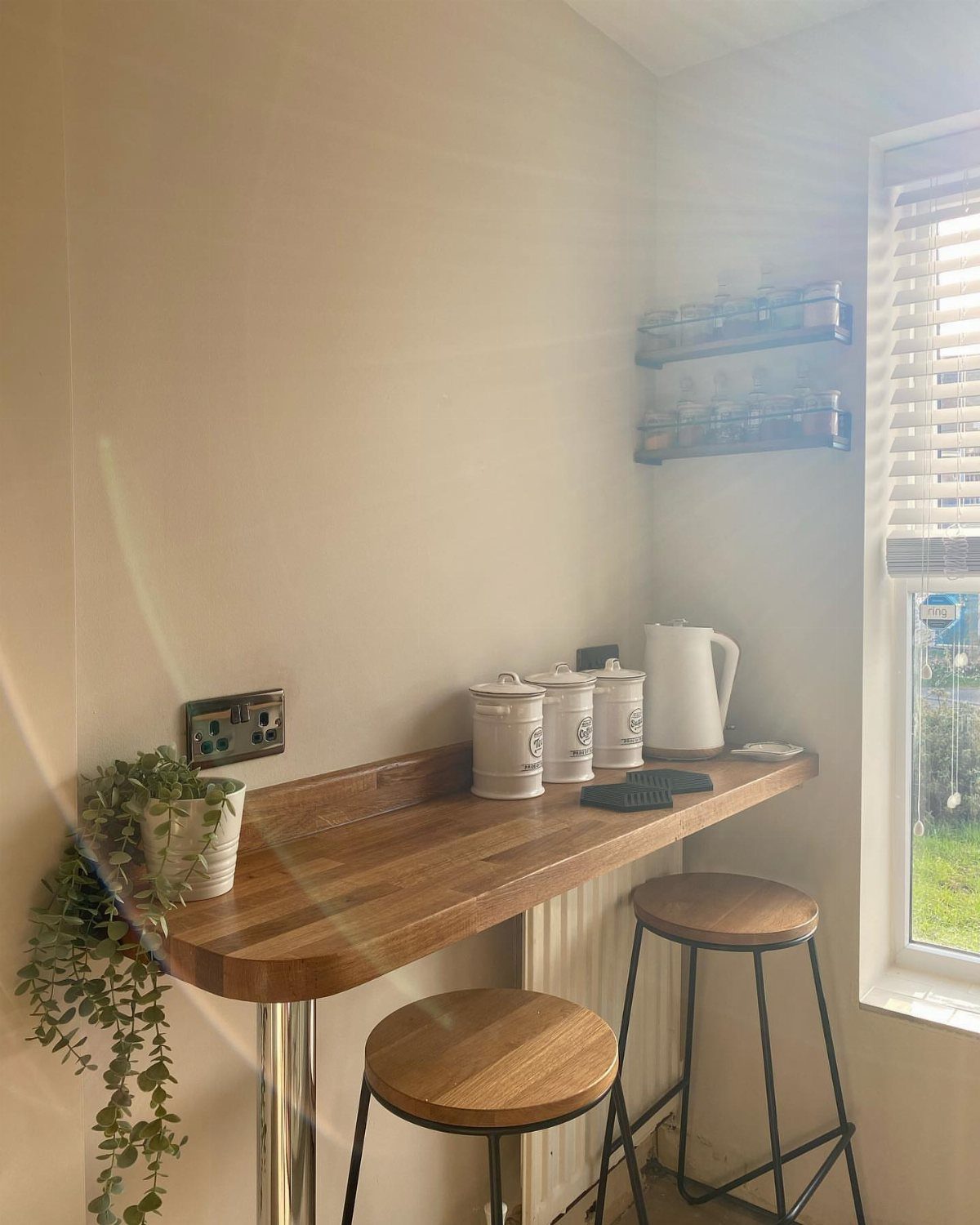 18 Small Kitchen Remodel Ideas to Open Up Your Space 15 Wooden breakfast bar with two stools, white canisters, and a kettle by a window.