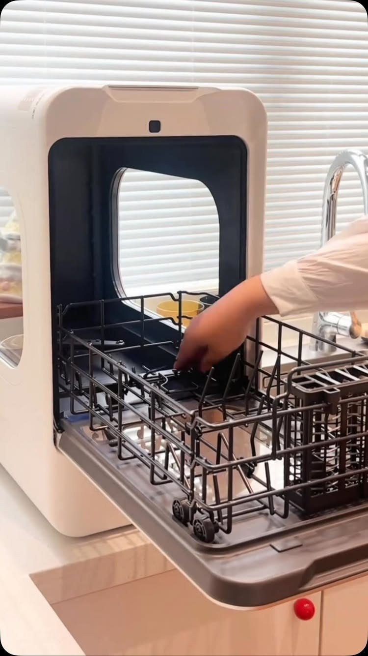 18 Small Kitchen Remodel Ideas to Open Up Your Space 5 A person reaching into a small, white compact dishwasher sitting on a kitchen counter.