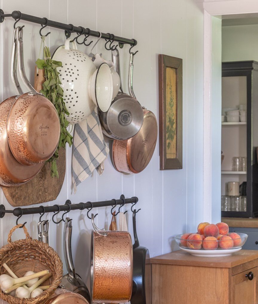 18 Small Kitchen Remodel Ideas to Open Up Your Space 11 Copper pots and kitchen utensils hanging from black metal rails on a white wall.