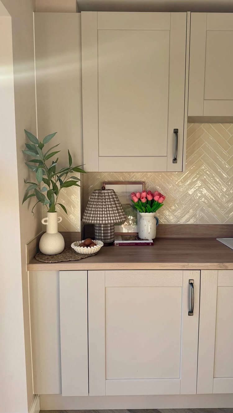 18 Small Kitchen Remodel Ideas to Open Up Your Space 6 Beige herringbone tile backsplash behind a wooden kitchen countertop with decorative vases and a lamp.
