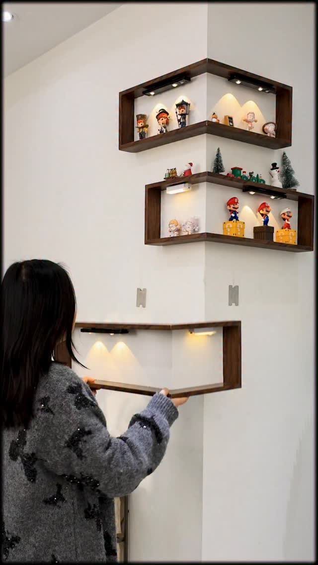12 Storage Ideas for Small Homes to Add Extra Space Fast 8 A person installing dark wooden corner shelves with integrated lighting on a white wall.