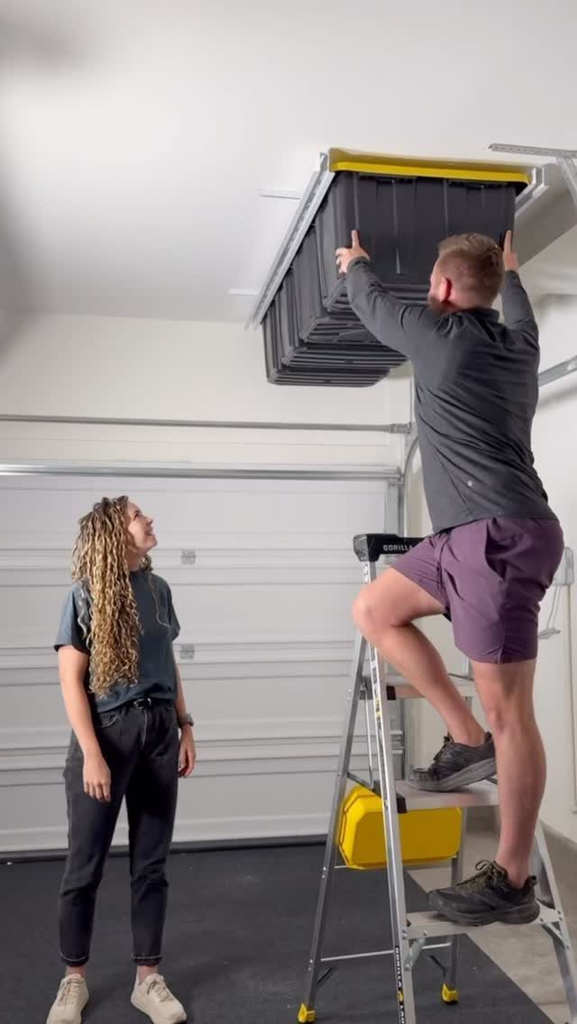 12 Storage Ideas for Small Homes to Add Extra Space Fast 6 A man on a ladder installing large black storage bins to a garage ceiling.