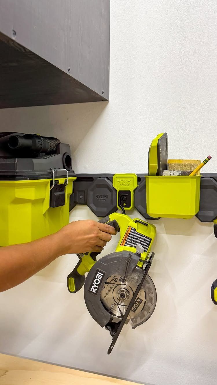 Tool Wall Storage: 8 Ideas for Garage and Workshop 6 A hand reaches for a Ryobi circular saw hanging on a modular wall storage system.