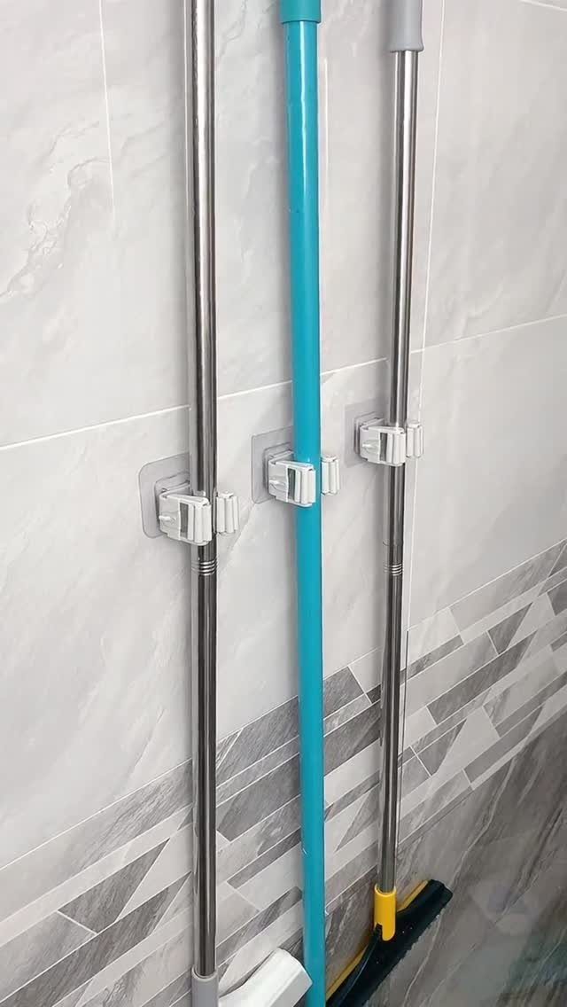 Tool Wall Storage: 8 Ideas for Garage and Workshop 4 Three white wall-mounted holders securing the handles of a mop and brooms against a tiled wall.