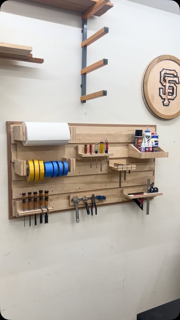 Tool Wall Storage: 8 Ideas for Garage and Workshop 8 A wooden slatwall organizer holding workshop tools, tapes, and various small supplies on a white wall.