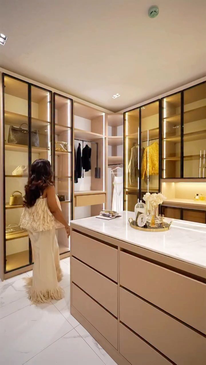 Walk in Closet Storage: 9 Ideas That Work in Real Homes 9 A woman stands in a luxury walk-in closet with glass cabinets and a marble island.