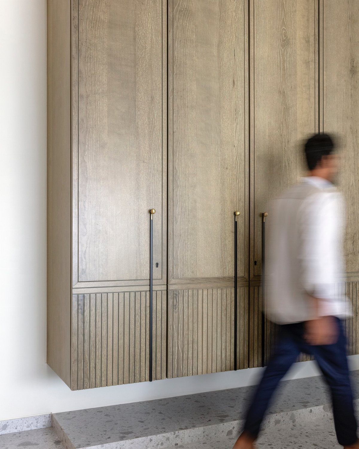 14 Wardrobe Interior Design Ideas for Every Bedroom 11 Light wood grain floating wardrobe with long black handles mounted on a white wall.