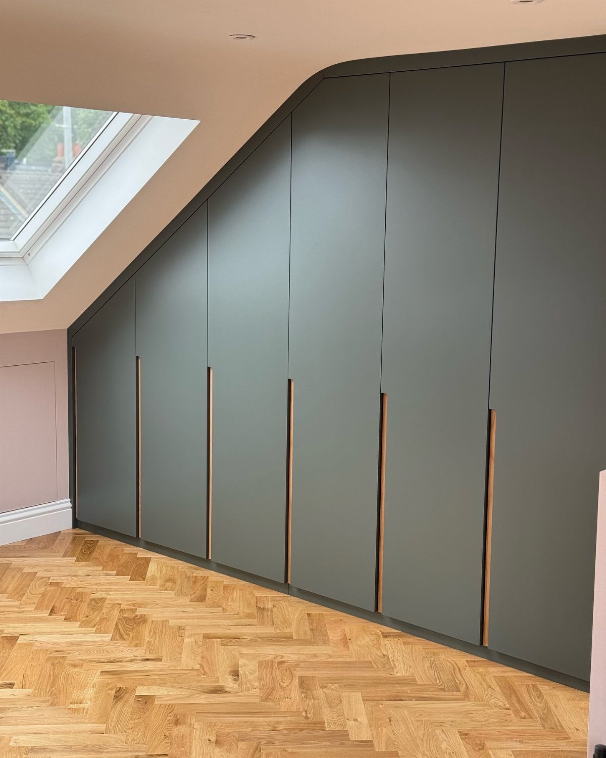 14 Wardrobe Interior Design Ideas for Every Bedroom 12 Grey built-in wardrobe with long wooden handles installed under a sloped ceiling with a skylight.